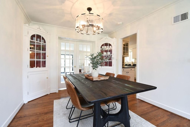 dining room featuring an inviting chandelier, dark wood-type flooring, crown molding, and visible vents