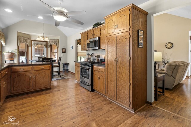 kitchen with lofted ceiling, dark countertops, stainless steel appliances, light wood-type flooring, and ceiling fan with notable chandelier