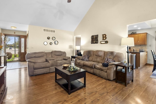 living area featuring a ceiling fan, high vaulted ceiling, light wood-style flooring, and visible vents