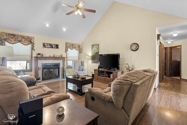 living area with a tiled fireplace, high vaulted ceiling, wood finished floors, and ceiling fan