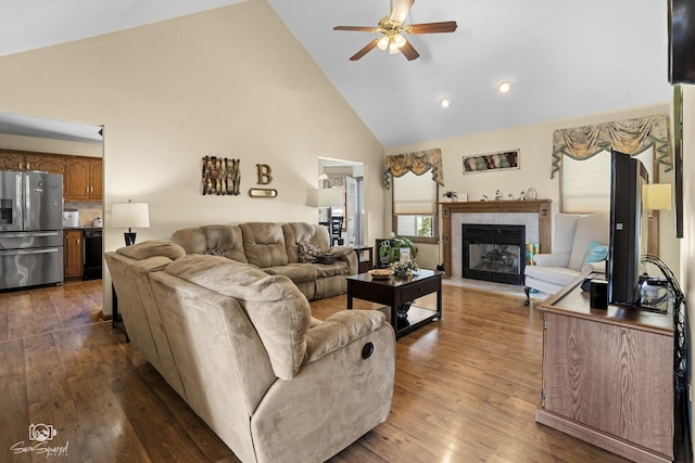 living room featuring a tiled fireplace, high vaulted ceiling, a ceiling fan, and dark wood-style flooring