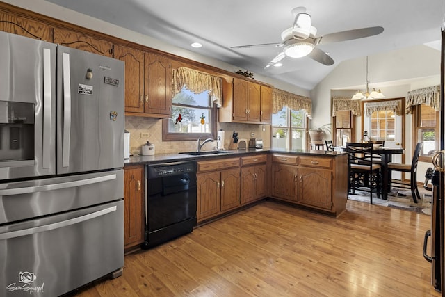 kitchen with stainless steel fridge, ceiling fan with notable chandelier, dark countertops, dishwasher, and a sink