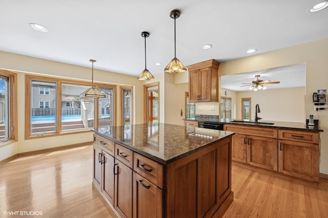 kitchen with a kitchen island, hanging light fixtures, brown cabinets, a sink, and light wood finished floors