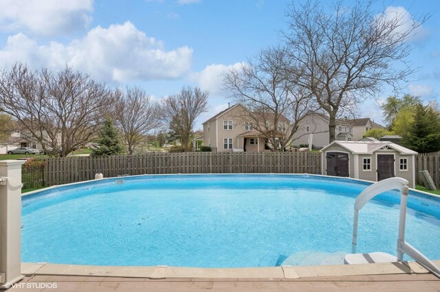 view of swimming pool featuring a fenced backyard, a fenced in pool, an outbuilding, and a residential view