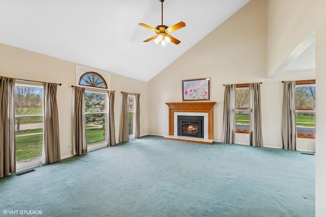 unfurnished living room with carpet flooring, ceiling fan, a warm lit fireplace, high vaulted ceiling, and a healthy amount of sunlight