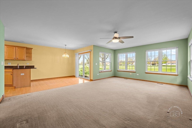 21600 W Larch Dr, Plainfield, IL 60544 - unfurnished living room featuring light wood-style flooring, baseboards, visible vents, ceiling fan with notable chandelier, and light carpet