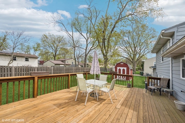 wooden deck featuring a fenced backyard, a shed, a lawn, an outbuilding, and outdoor dining space