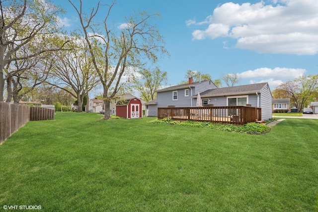 back of property featuring fence, a wooden deck, a yard, a storage shed, and an outbuilding