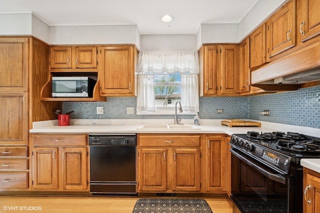 kitchen featuring brown cabinetry, light countertops, under cabinet range hood, a sink, and black appliances