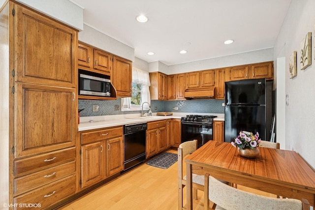 kitchen featuring brown cabinets, light countertops, light wood-type flooring, backsplash, and black appliances
