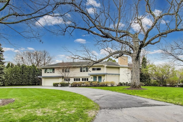view of front of house with an attached garage, a front yard, driveway, and a chimney