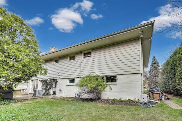 back of house with central AC, a patio, a chimney, brick siding, and a lawn