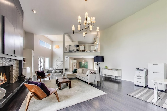 living room featuring a high ceiling, a notable chandelier, a fireplace, wood finished floors, and stairway