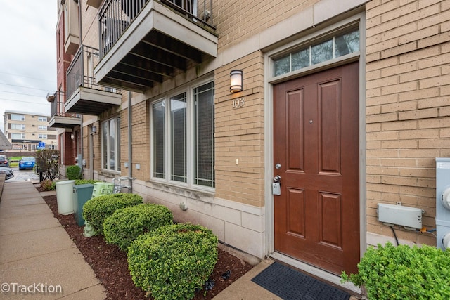 view of exterior entry featuring brick siding and a balcony