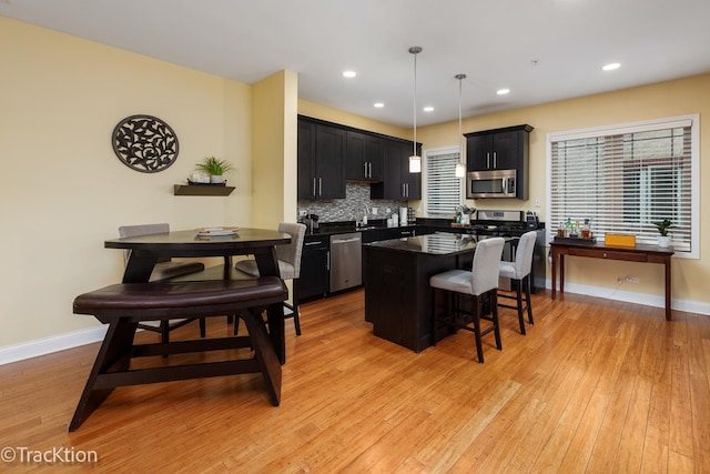 kitchen with a kitchen breakfast bar, dark countertops, appliances with stainless steel finishes, a center island, and light wood finished floors