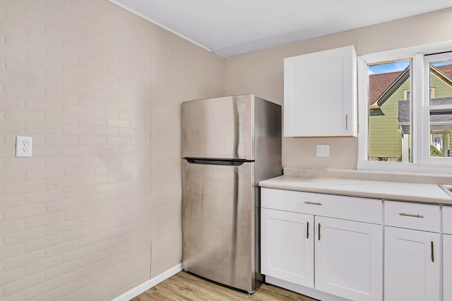 kitchen with light wood-style flooring, light countertops, white cabinets, and freestanding refrigerator