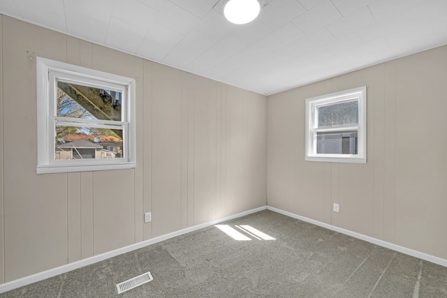 unfurnished room with visible vents, plenty of natural light, a decorative wall, and carpet floors