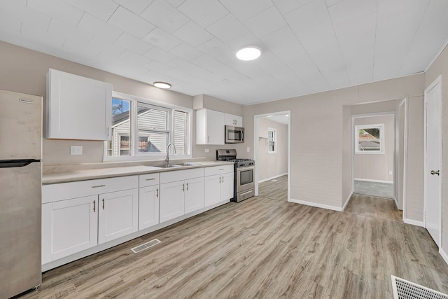 kitchen with appliances with stainless steel finishes, light countertops, light wood finished floors, a sink, and visible vents
