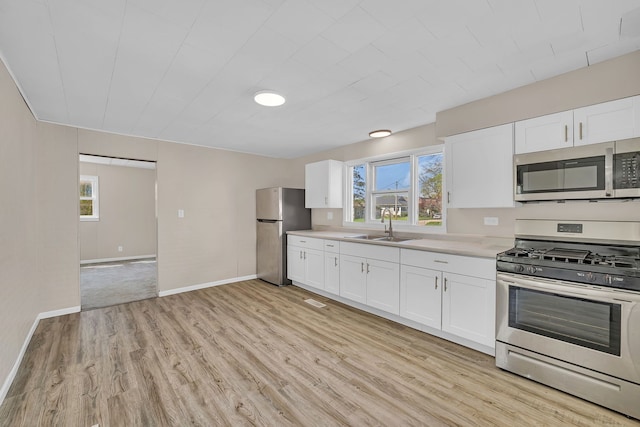 kitchen with a sink, stainless steel appliances, light wood-style floors, baseboards, and light countertops