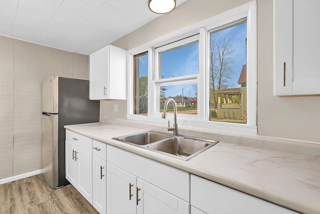 kitchen featuring freestanding refrigerator, light countertops, white cabinets, a sink, and light wood-type flooring