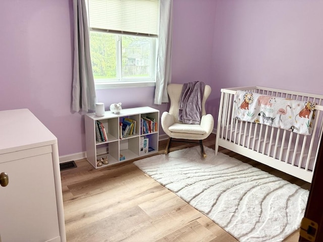 bedroom featuring baseboards, a crib, and wood finished floors