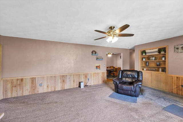sitting room featuring wood walls, built in features, ceiling fan, carpet floors, and wainscoting