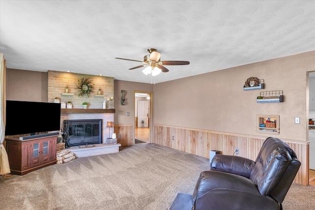 carpeted living area with a fireplace, ceiling fan, wood walls, and a wainscoted wall