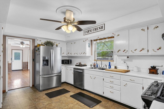 kitchen featuring a sink, white cabinets, ceiling fan, backsplash, and appliances with stainless steel finishes