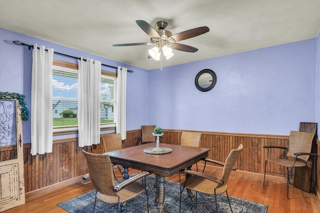 dining space featuring wood walls, ceiling fan, a wainscoted wall, and wood finished floors