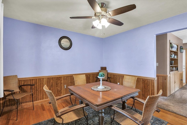 dining space featuring wood walls, wainscoting, ceiling fan, and wood finished floors