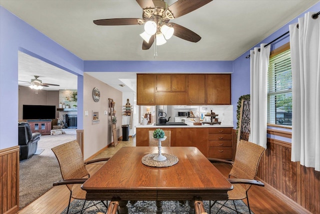 dining area featuring a large fireplace, baseboards, light wood-style flooring, and a ceiling fan