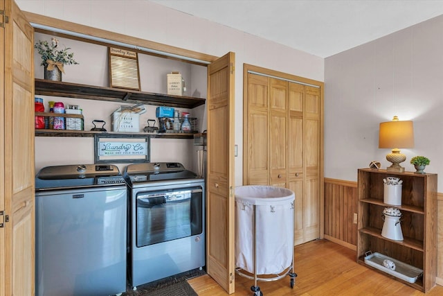 washroom with wood walls, a wainscoted wall, laundry area, washer and dryer, and light wood-style flooring