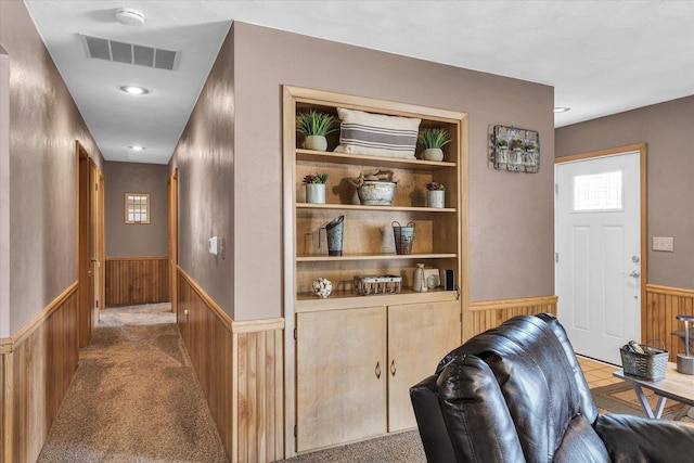 corridor featuring wooden walls, built in features, visible vents, and a wainscoted wall