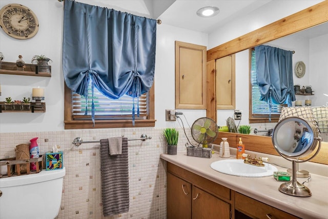 bathroom with tile walls, toilet, vanity, and a wainscoted wall