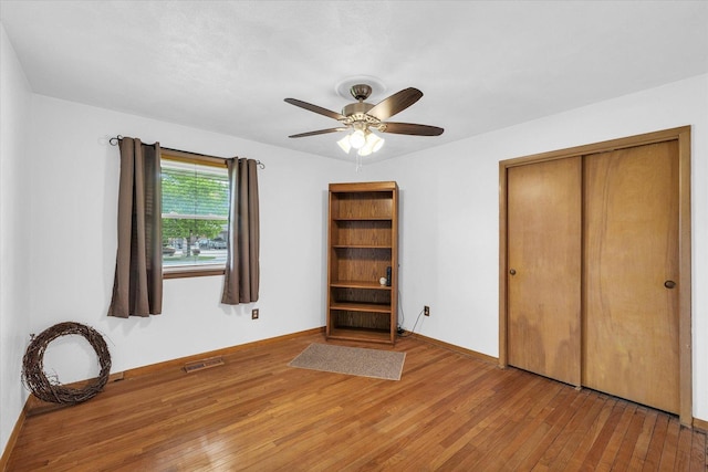unfurnished bedroom with a closet, hardwood / wood-style floors, visible vents, a ceiling fan, and baseboards