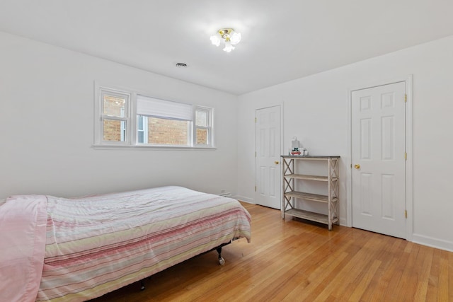 bedroom with baseboards, visible vents, and light wood finished floors