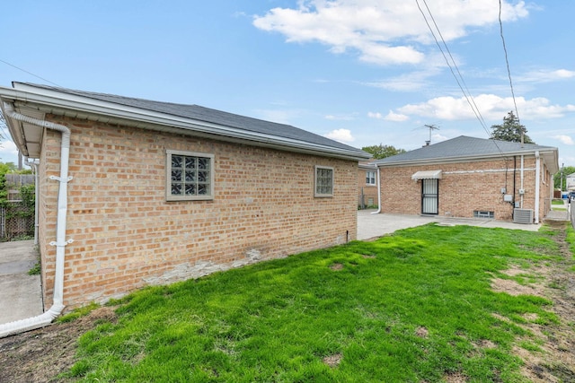 rear view of house featuring a lawn, central AC unit, a patio area, and brick siding
