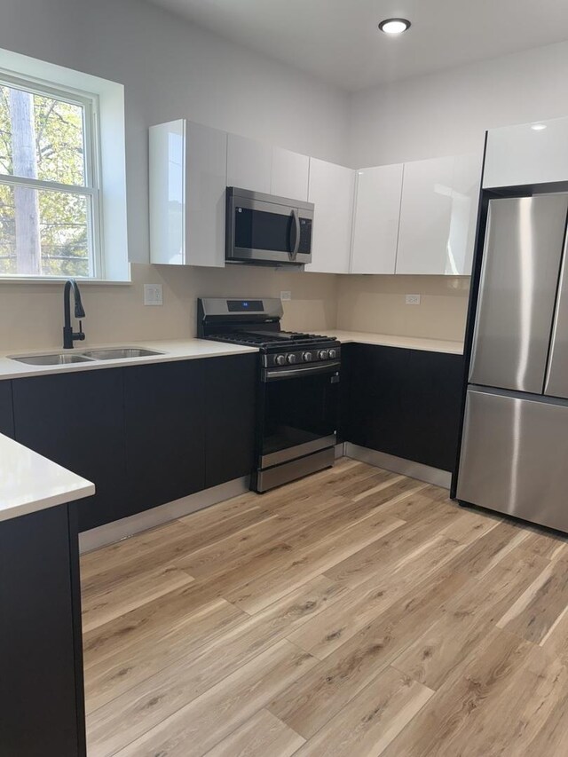 kitchen with appliances with stainless steel finishes, light countertops, a sink, light wood-type flooring, and modern cabinets