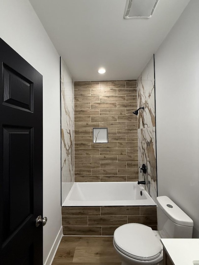 full bath with recessed lighting, wood finished floors, tiled shower / bath combo, toilet, and vanity