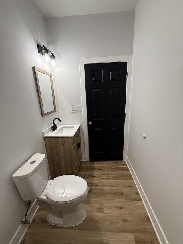 half bathroom with toilet, vanity, wood finished floors, and baseboards