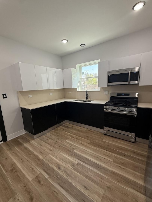 kitchen with light wood-style floors, appliances with stainless steel finishes, light countertops, dark cabinetry, and white cabinetry