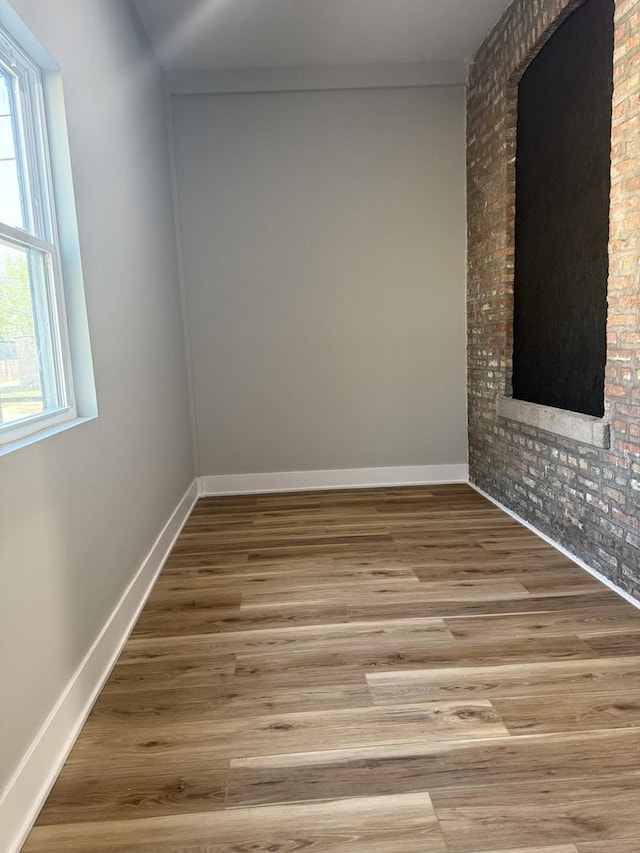 empty room with brick wall, a wealth of natural light, wood finished floors, and baseboards