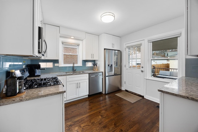 kitchen featuring dark wood-style flooring, light stone countertops, appliances with stainless steel finishes, a sink, and white cabinetry