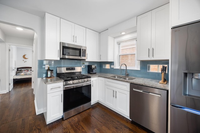 kitchen featuring a sink, appliances with stainless steel finishes, light stone countertops, and dark wood-style floors
