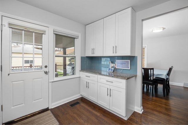 kitchen with visible vents, tasteful backsplash, light stone countertops, dark wood finished floors, and baseboards