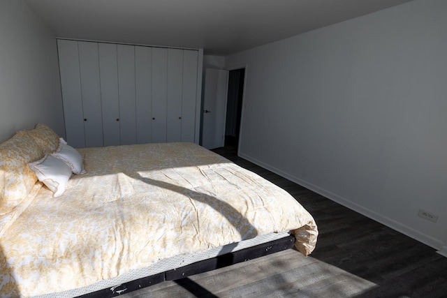 bedroom with a closet, dark wood-style flooring, and baseboards