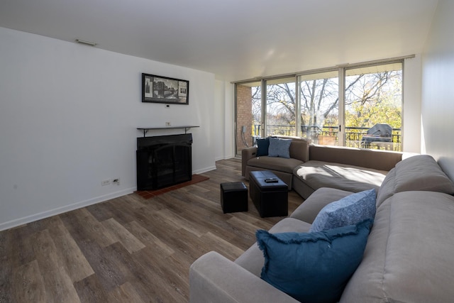 living room featuring wood finished floors, visible vents, a fireplace with raised hearth, and baseboards