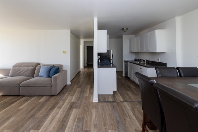 kitchen featuring white cabinets, a sink, dark countertops, stainless steel appliances, and open floor plan