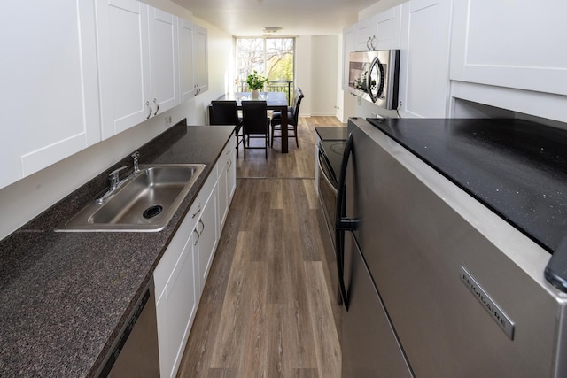 kitchen featuring stainless steel microwave, dark countertops, dark wood-style flooring, a sink, and white cabinetry
