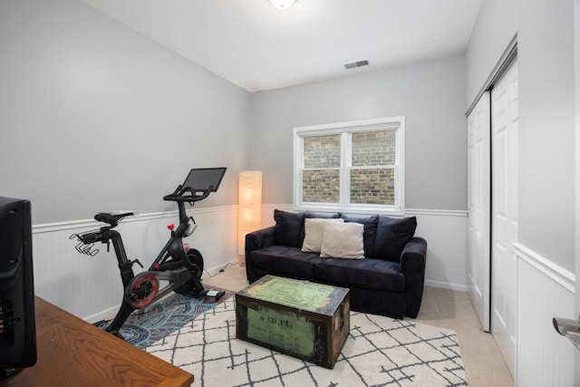 sitting room featuring visible vents, light carpet, and a wainscoted wall